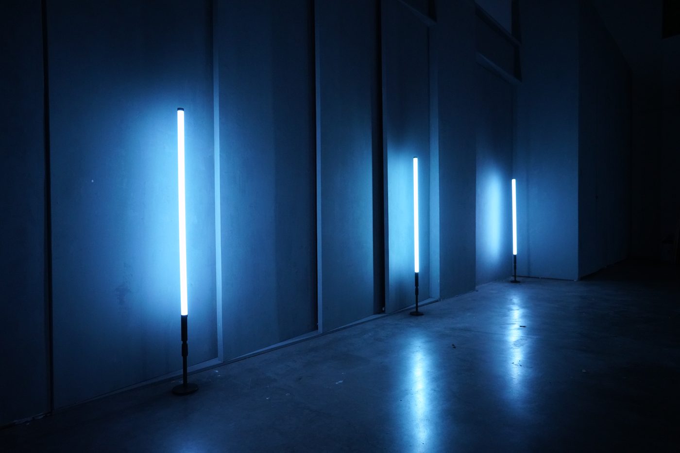Sci-fi warehouse standing set: raw concrete walls and a polished floor lit by glowing blue tube lights